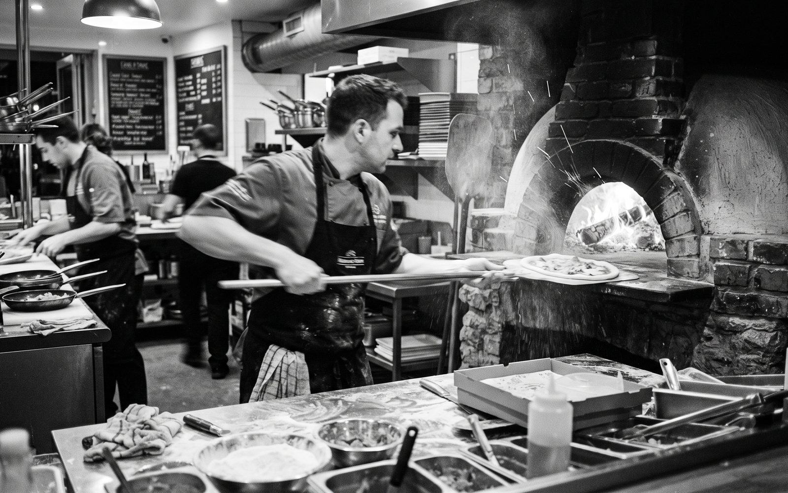 Koch schiebt eine Pizza in den gemauerten Holzofen